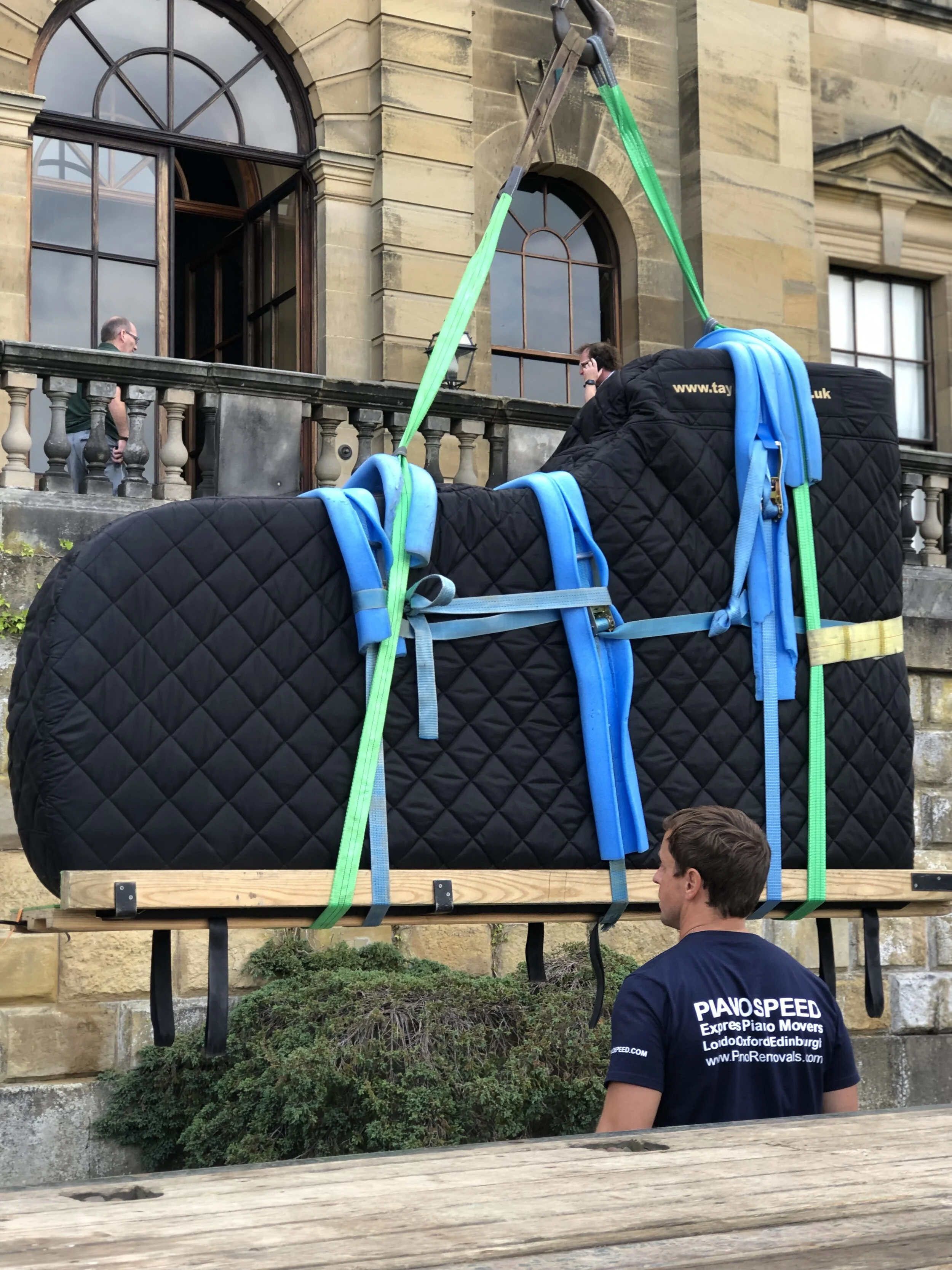 Concert grand piano lifted on padded straps by a specialist crew